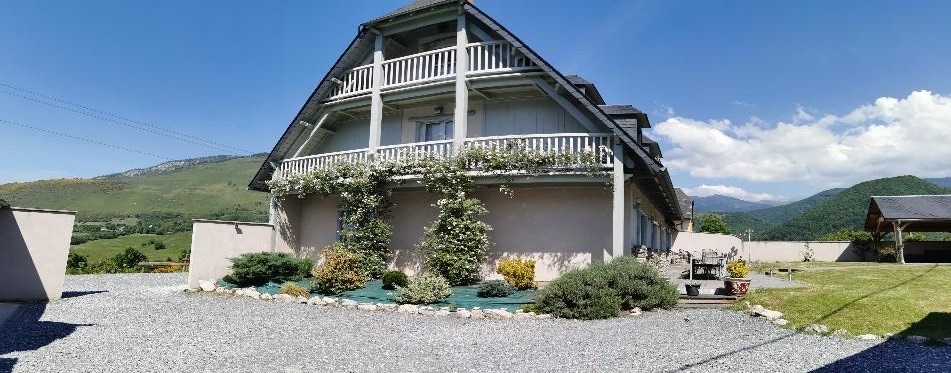 Les Écuries de Lisa — a large chalet with white balconies on the heights of Arreau, mountains behind